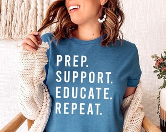 Może przedstawiać: Kobieta w niebieskiej koszulce z napisem "PREP. SUPPORT. EDUCATE. REPEAT." w białym kolorze. Siedzi na krześle z białym dzianym narzutem na ramionach.