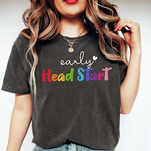 May include: A dark gray t-shirt with the text "early Head Start" in rainbow colors. The text is stylized with a heart after the word "early" and a rainbow pattern on the letters.