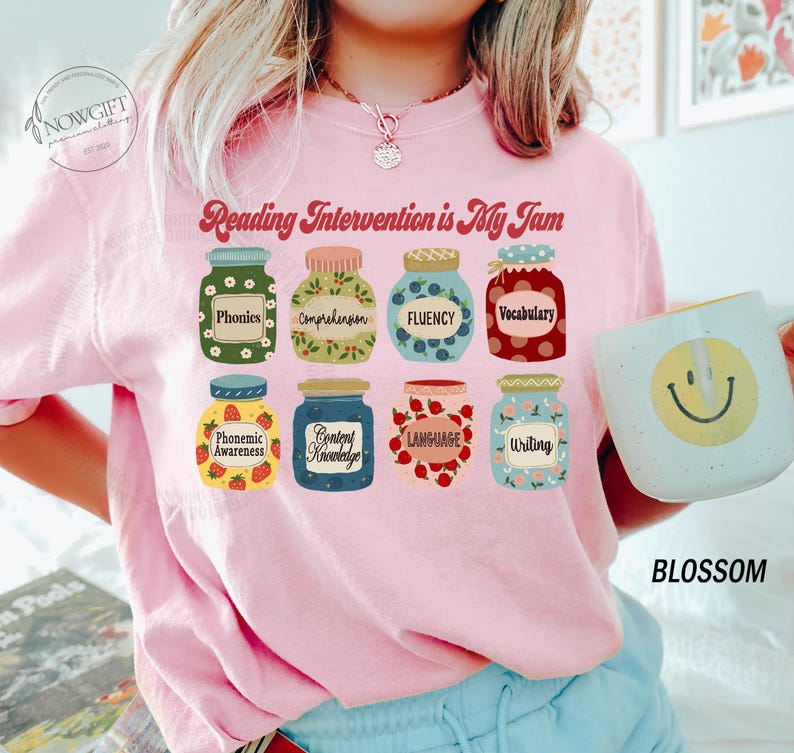 May include: Pink t-shirt with the text "Reading Intervention is My Jam" and a graphic of jars with different reading skills listed on them, such as "Phonics", "Comprehension", "Fluency", and "Vocabulary".