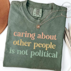 May include: A green t-shirt with the text "caring about other people is not political" printed in pink, orange, and green.
