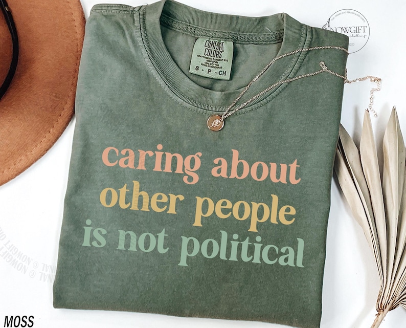 May include: A green t-shirt with the text "caring about other people is not political" printed in pink, orange, and green.