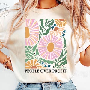 May include: A white t-shirt with a floral design and the text "PEOPLE OVER PROFIT" printed on the front. The flowers are pink, orange, and yellow.