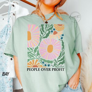 May include: A light green t-shirt with a floral design and the text "People Over Profit" printed on the front.