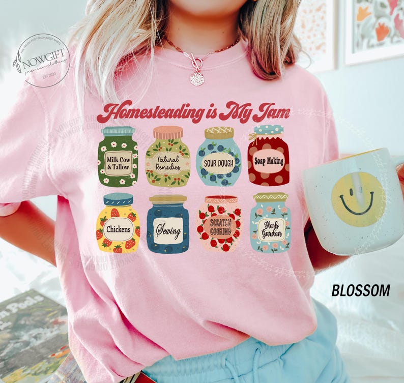 May include: Pink crewneck sweatshirt with the text "Homesteading is My Jam" and illustrations of jars labeled with homesteading activities. A mug with a smiley face is held in the image.