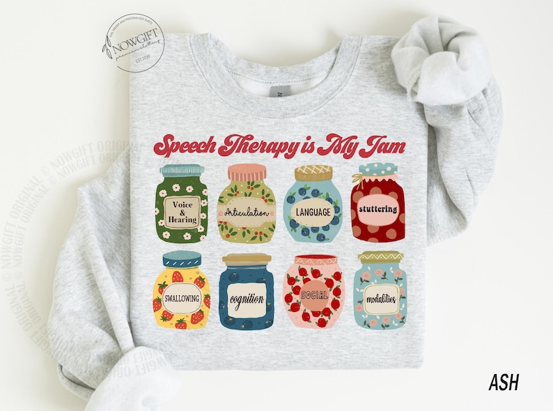 May include: A light gray sweatshirt with the text "Speech Therapy is My Jam" printed in red. The text is surrounded by illustrations of jars with different speech therapy related terms, such as "Voice & Hearing", "Articulation", "Language", "Stuttering", "Swallowing", "Cognition", "Social", and "Modalities".