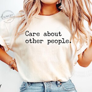 Puede incluir: Una camiseta blanca con el texto "Care about other people." impreso en negro. La camiseta la lleva puesta una persona con el pelo largo y rubio. El fondo es blanco.