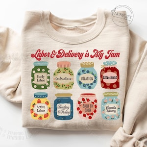 May include: A beige sweatshirt with the text "Labor & Delivery is My Jam" printed in red. The text is surrounded by nine illustrated jars with different stages of labor printed on them.