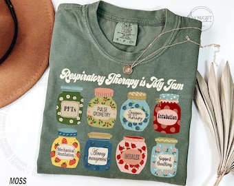 May include: Moss green t-shirt with the text "Respiratory Therapy is My Jam." The shirt features colorful illustrations of jars labeled with respiratory therapy terms such as "PFTs" and "Intubation."
