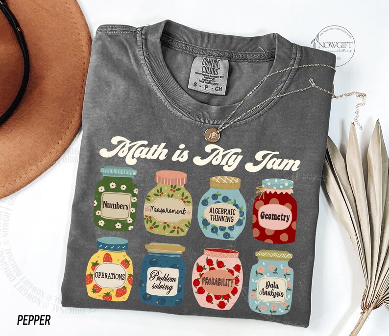 May include: Gray t-shirt with the text "Math is My Jam" in a retro font. The shirt features a design of eight jars with different math-related terms, such as "Numbers", "Measurement", "Algebraic Thinking", and "Geometry".