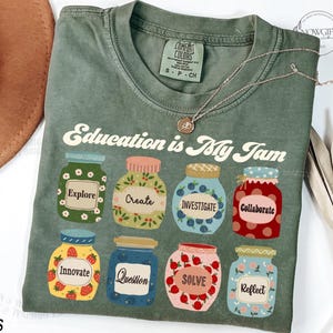 May include: Green t-shirt with the text "Education is My Jam" and a design of jars with different words on them, including "Explore", "Create", "Investigate", "Collaborate", "Innovate", "Question", "Solve", and "Reflect".