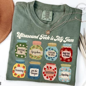 Könnte beinhalten: Ein grünes T-Shirt mit dem Text "Ultrasound Tech is My Jam" in einer Retro-Schrift. Das Shirt zeigt ein Design aus neun Gläsern mit verschiedenen Sätzen, die sich auf die Ultraschalltechnologie beziehen, wie z. B. "Setting Up", "Lying Down", "Exposing the Area", "Cold Gel & Probe", "Scanning", "Get the Images", "Questions" und "Reporting".