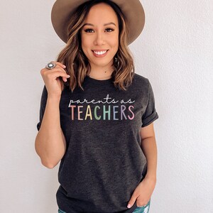 Puede incluir: Una camiseta gris oscuro con el texto "parents as TEACHERS" en colores arco&iacute;ris.