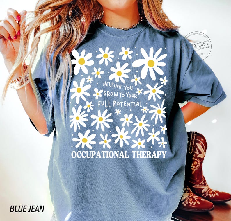 May include: Blue jean colored t-shirt with a daisy flower design. The shirt has the text "Helping You Grow To Your Full Potential" and "Occupational Therapy" in white. The shirt is a comfortable, casual style.
