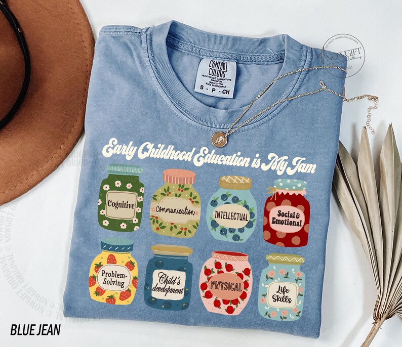 Puede incluir: Una camiseta de mezclilla azul con el texto "Early Childhood Education is My Jam" e ilustraciones de frascos con diferentes aspectos del desarrollo de la primera infancia, como la cognici&oacute;n, la comunicaci&oacute;n, la inteligencia, lo social y lo emocional, la resoluci&oacute;n de problemas, el desarrollo del ni&ntilde;o, lo f&iacute;sico y las habilidades para la vida.