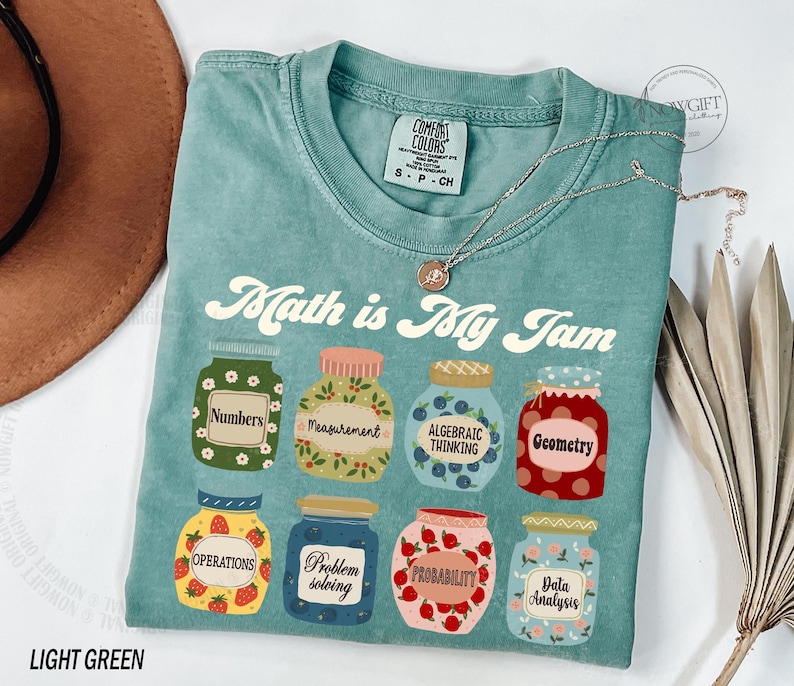 May include: Light green t-shirt with the text "Math is My Jam" printed on the front. The text is in a retro font and is surrounded by illustrations of jars with different math-related themes, such as "Numbers", "Measurement", "Algebraic Thinking", "Geometry", "Operations", "Problem Solving", "Probability", and "Data Analysis".