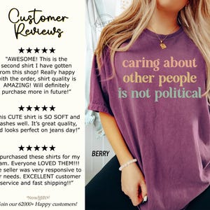 May include: A purple t-shirt with the text "caring about other people is not political" in colorful letters. The shirt is being worn by a person with a bracelet on their wrist. Customer reviews are shown on the left side of the image.