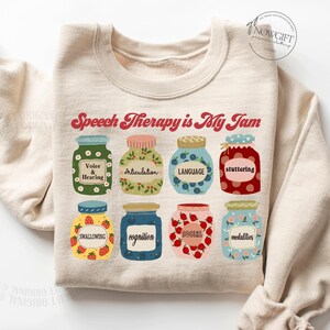 May include: A beige sweatshirt with the text "Speech Therapy is My Jam" in red and white. The text is surrounded by nine illustrated jars of jam, each with a different speech therapy topic written on the label.