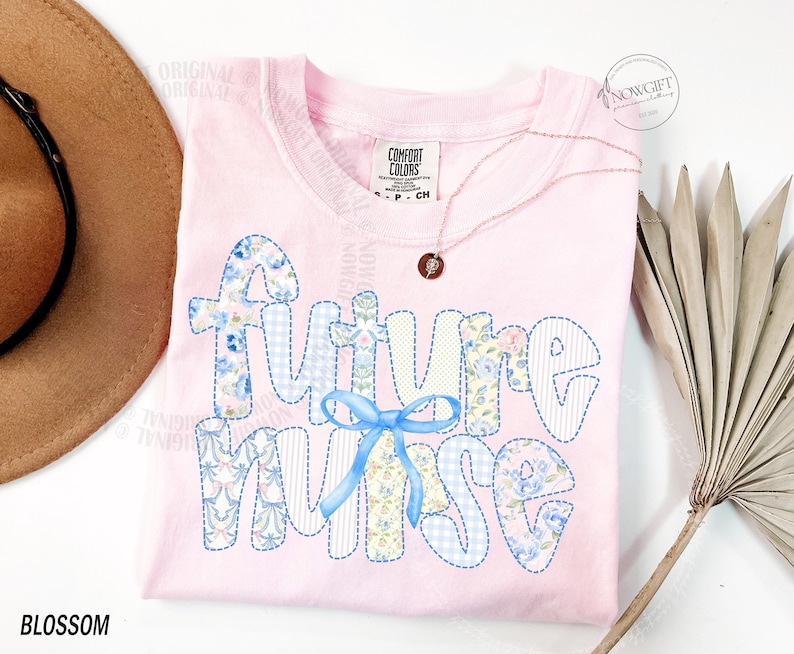 May include: A light pink t-shirt with the words "FUTURE NURSE" in a patchwork design with blue floral and gingham patterns. A blue bow is centered below the word "FUTURE". A gold necklace with a small pendant is draped on the shirt.