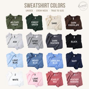 May include: A chart showing 16 different sweatshirt colors. The colors are: Military Green, Forest Green, Sand, Dark Chocolate, Ash, Sport Grey, Dark Heather, Black, Light Blue, Indigo Blue, Carolina Blue, Navy, White, Light Pink, Scarlet Red, and Heather Maroon.