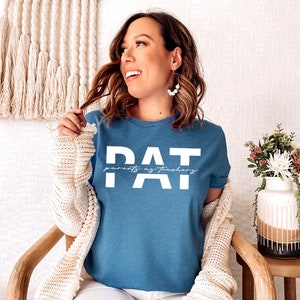 May include: A blue t-shirt with the text "PAT" in white letters. The text "parents as teachers" is written in smaller white letters below the "PAT".
