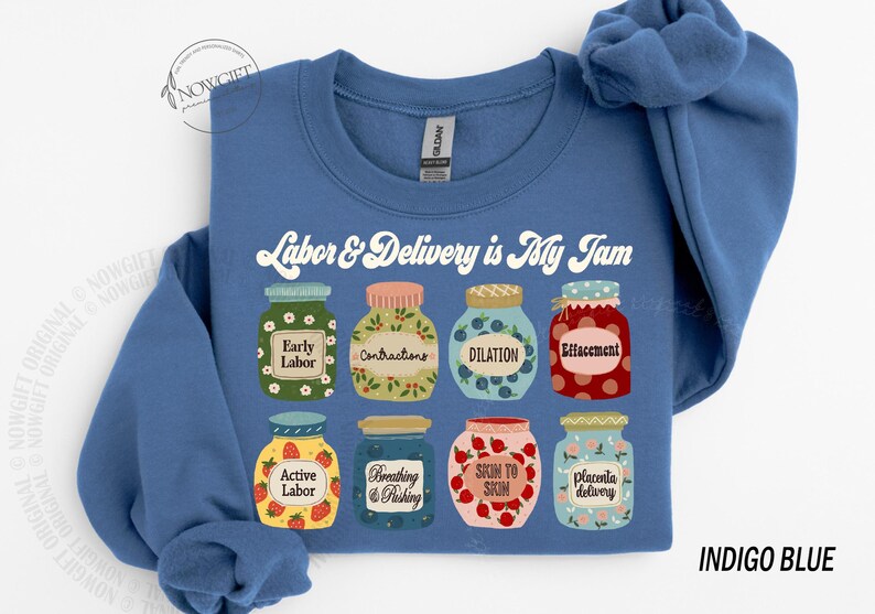 May include: Indigo blue sweatshirt with the text "Labor & Delivery is My Jam" in white. The sweatshirt features a graphic of nine jars with different stages of labor and delivery, such as "Early Labor", "Contractions", "Dilation", and "Placenta Delivery".