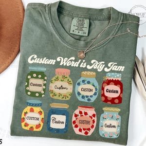 Könnte beinhalten: Ein grünes T-Shirt mit dem Aufdruck "Custom Word is My Jam". Der Text ist von Illustrationen von Gläsern mit dem Wort "Custom" umgeben.