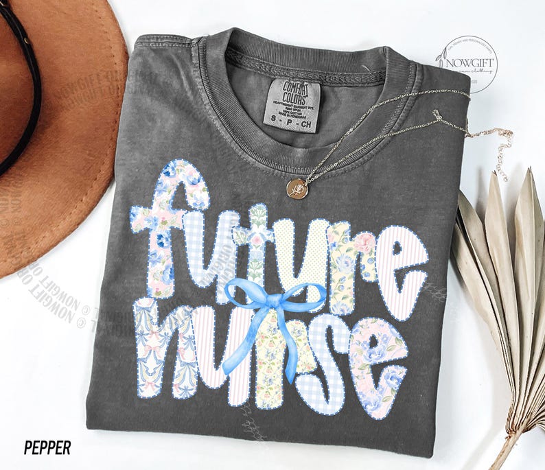 May include: A gray t-shirt with the words "future nurse" in a patchwork design with floral and gingham patterns. A light blue bow accents the word "nurse". A gold necklace with a pendant is on the shirt.