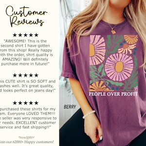 May include: Purple t-shirt with a floral design and the text "PEOPLE OVER PROFIT". The shirt is made of a soft, comfortable material and has a relaxed fit.