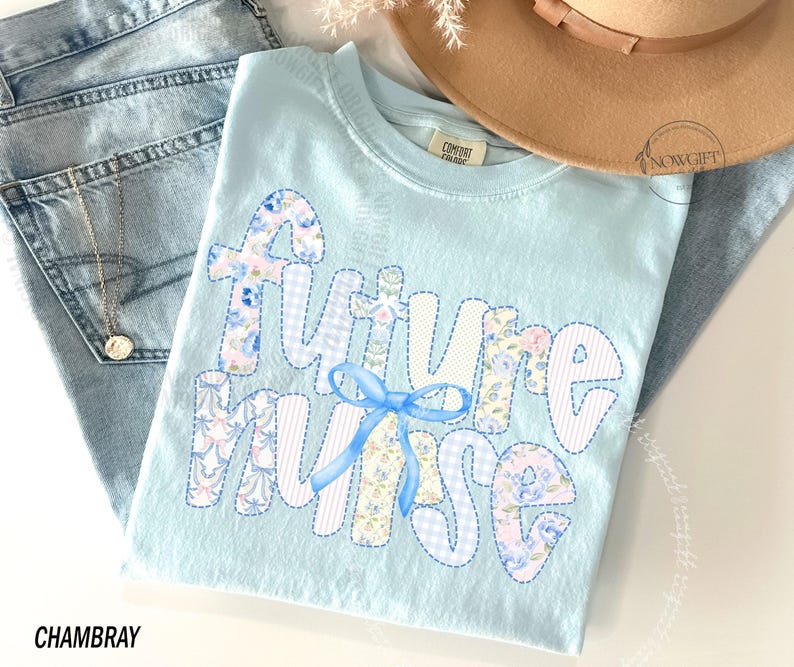 May include: A light blue t-shirt with the words "Future Nurse" appliqued in a patchwork style. The letters are in various floral and patterned fabrics, with a blue bow. The shirt is folded on top of a pair of blue jeans.
