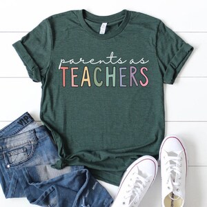 Puede incluir: Una camiseta verde oscuro con el texto "parents as TEACHERS" en colores arco&iacute;ris.