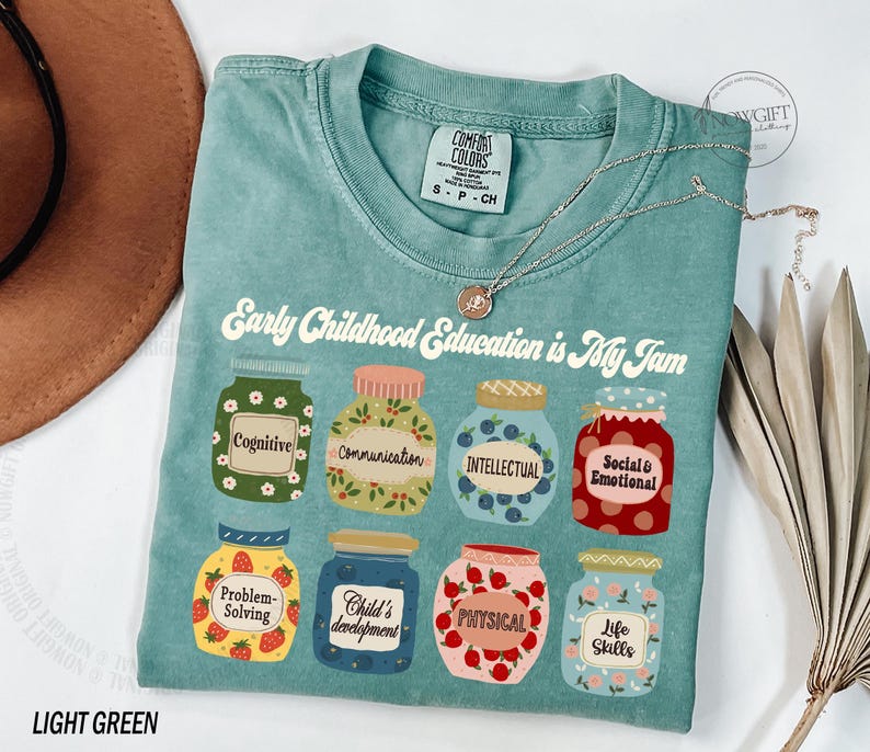 Puede incluir: Camiseta verde claro con el texto "Early Childhood Education is My Jam" impreso en la parte delantera. El texto est&aacute; rodeado de ilustraciones de frascos con diferentes etiquetas, que incluyen "Cognitive", "Communication", "Intellectual", "Social & Emotional", "Problem-Solving", "Child's Development", "Physical" y "Life Skills".