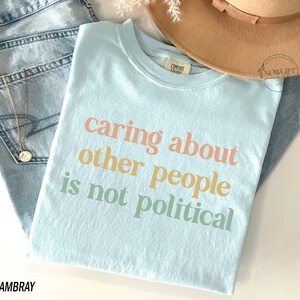 May include: A light blue t-shirt with the text "caring about other people is not political" printed in a rainbow color scheme.
