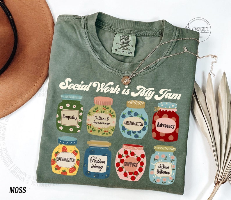 May include: A green t-shirt with the text "Social Work is My Jam" in a retro font. The text is surrounded by illustrations of jars with different labels, including "Empathy", "Cultural Awareness", "Organization", "Advocacy", "Communication", "Problem Solving", "Support", and "Active Listener".