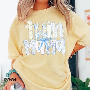 Puede incluir: Camiseta amarilla clara con la frase "Twin Mama" en un dise&ntilde;o de patchwork. Las letras est&aacute;n rellenas de estampados florales, cuadros y rayas, y presenta un lazo azul. La camiseta es de estilo casual.