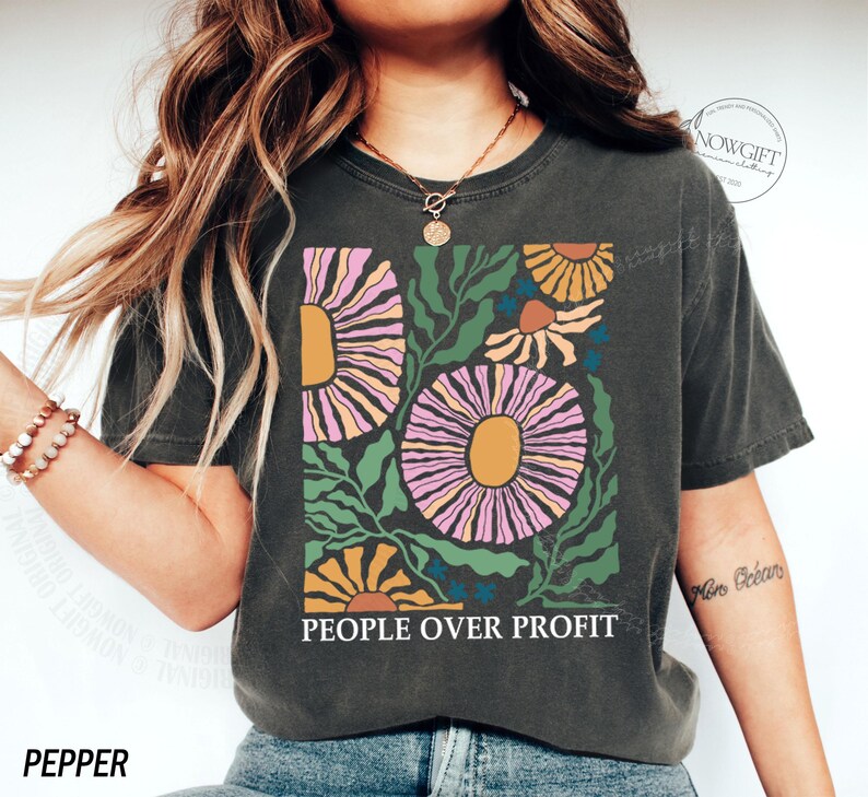 May include: A dark gray t-shirt with a floral design in pink, yellow, and green. The text "PEOPLE OVER PROFIT" is printed on the shirt.