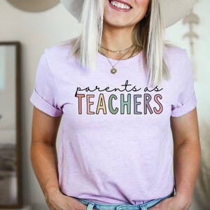 Puede incluir: Una camiseta de color morado claro con el texto "parents as TEACHERS" en colores arco&iacute;ris.