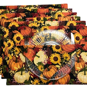 Op de afbeelding: Set van zes zwarte placemats met een herfstthema. De placemats hebben een herhalend patroon van zonnebloemen, pompoenen en herfstbladeren op een zwarte achtergrond. De placemats zijn afgewerkt met een bruine rand.