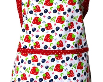 May include: A white apron with a red and white polka dot trim. The apron has a pocket and is decorated with a pattern of strawberries and blueberries.