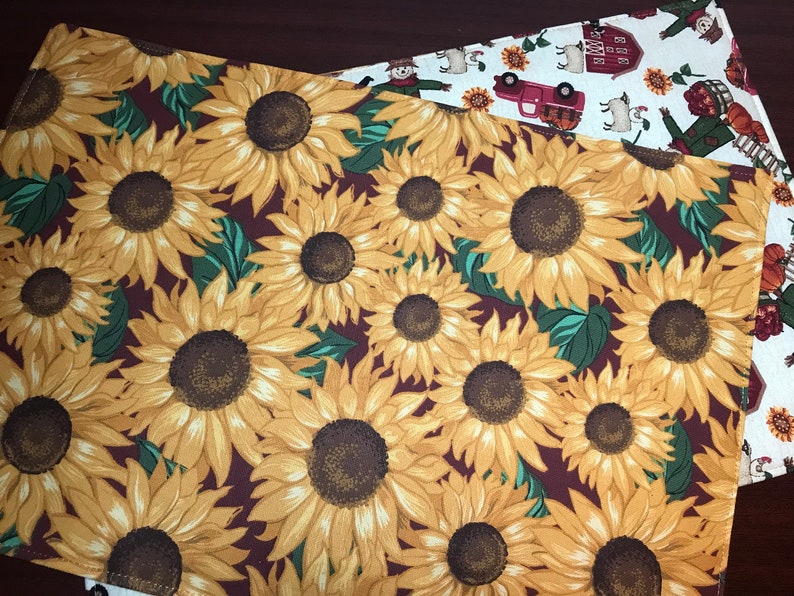 May include: A brown placemat with a pattern of yellow sunflowers on a burgundy background.