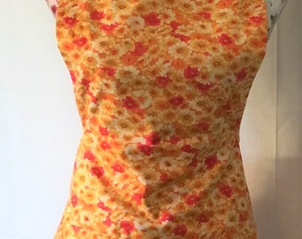 May include: A yellow and orange apron with a floral print. The apron has two pockets and a button closure.