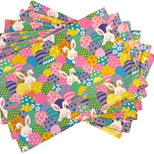 May include: A set of 8 pink placemats with a colorful Easter egg and bunny pattern. The placemats are made of fabric and feature a variety of colors, including pink, yellow, green, blue, and purple.