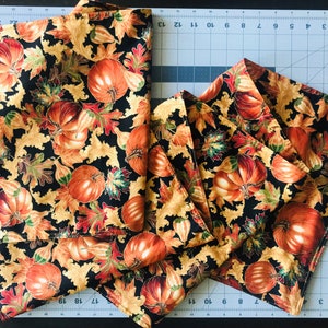 May include: A set of six black fabric napkins with a gold and orange pumpkin and leaf pattern.