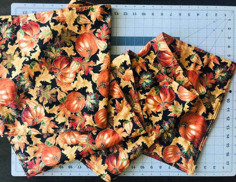 May include: A set of six black fabric napkins with a gold and orange pumpkin and leaf pattern.