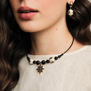 May include: A black and white beaded choker necklace with a gold star pendant. The necklace is made of black and white beads with a gold star pendant in the center. The star pendant has a black center and gold points.