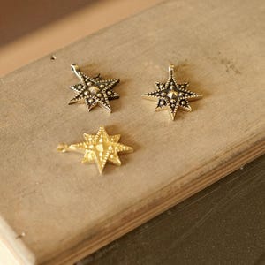 Three small star-shaped brass charms with detailed geometric engraving, shown in antique gold and darker brass tones, arranged on a wooden work surface under warm natural light.