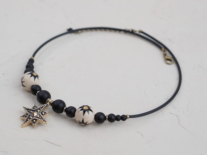 May include: A black choker necklace with black and white beads and a gold star pendant.