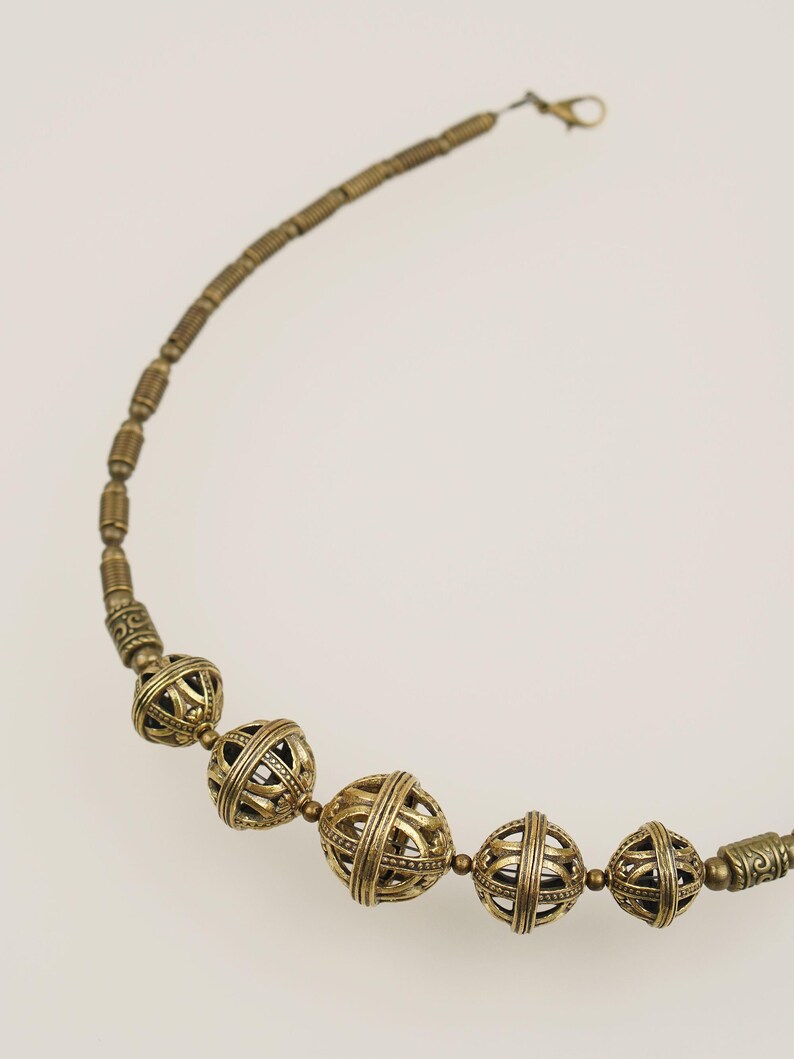 May include: A vintage-style necklace featuring a series of ornate, openwork metal beads in a warm, antique gold color. The necklace has a delicate chain and clasp, with the focal point being the spherical, cage-like beads.