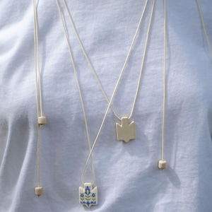Handmade ceramic wrap necklace featuring a hand-painted Ukrainian Trident pendant with traditional folk flower design in blue.