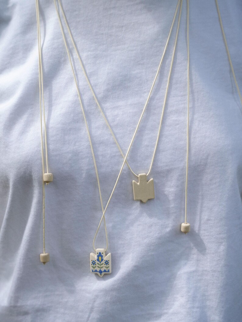 Handmade ceramic wrap necklace featuring a hand-painted Ukrainian Trident pendant with traditional folk flower design in blue.