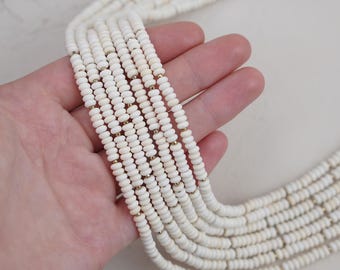 May include: A strand of white beads with gold accents. The beads are small and round, and they are strung together in a long, continuous strand.